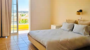 A bedroom with a bed, a nightstand, a wall-mounted lamp, and a view through a sliding glass door.