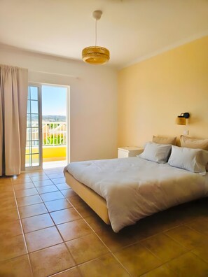 A bedroom with a bed, a nightstand, a wall-mounted lamp, and a view through a sliding glass door. - Three-Bedroom Villa with Sea View in Private Condominium, Pêra, Algarve (Pêra)