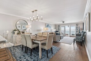 A spacious living area with a dining table, chairs, a chandelier, and a view through large windows. - Pier Pointe Oceanfront Condo in the Village, sleeps 4 (St Simons Island)