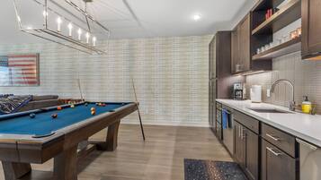 A modern kitchen with a pool table, wooden cabinets, and a coffee machine.
