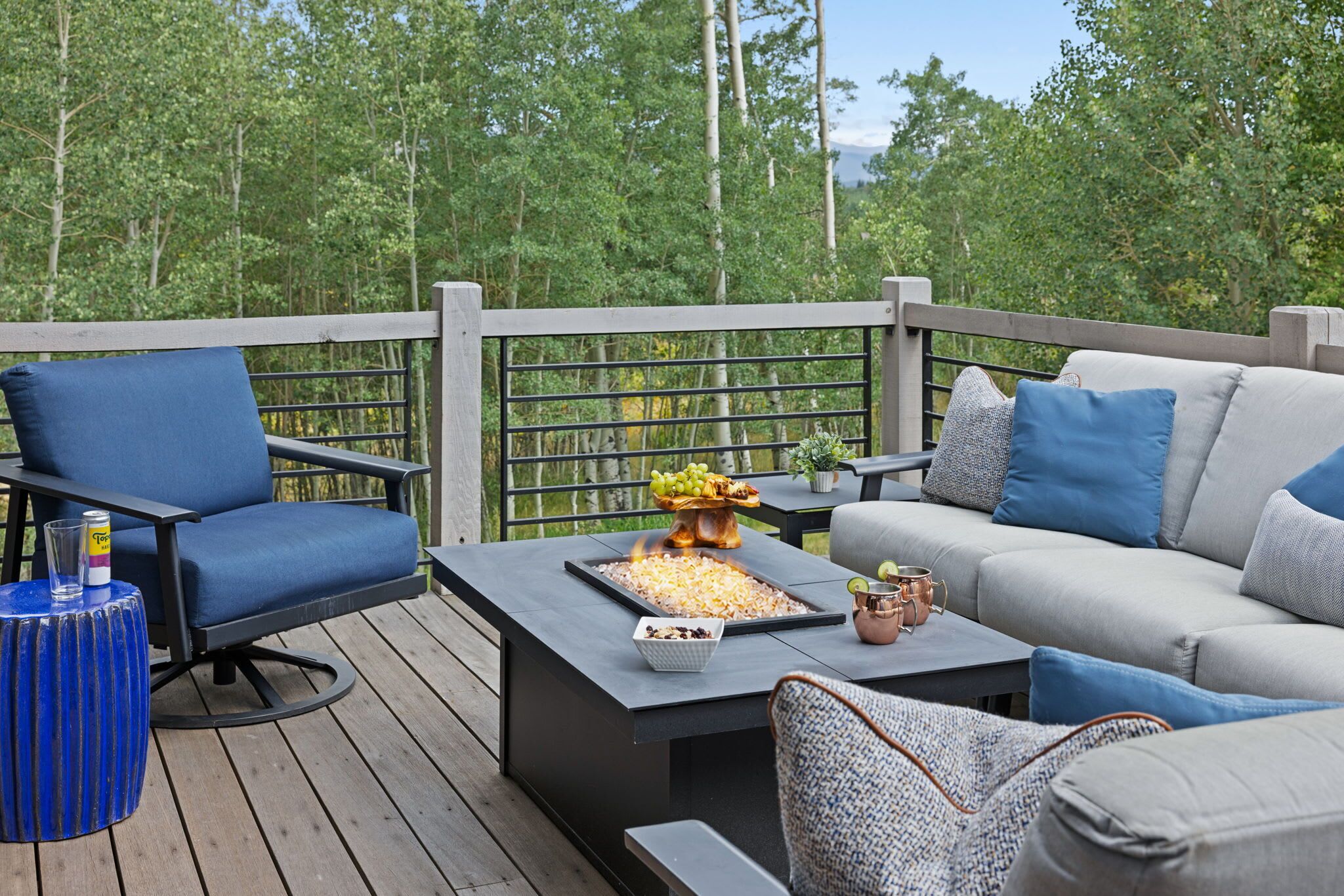 A deck with a fire feature, seating, and a table with drinks.