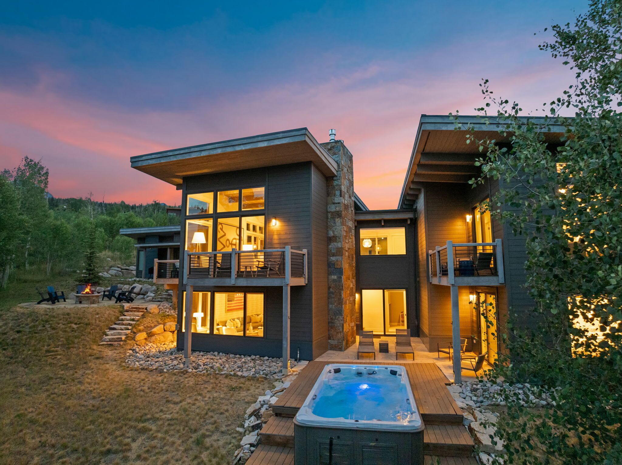 A modern two-story house with a hot tub, outdoor seating, and a view of the surrounding landscape.