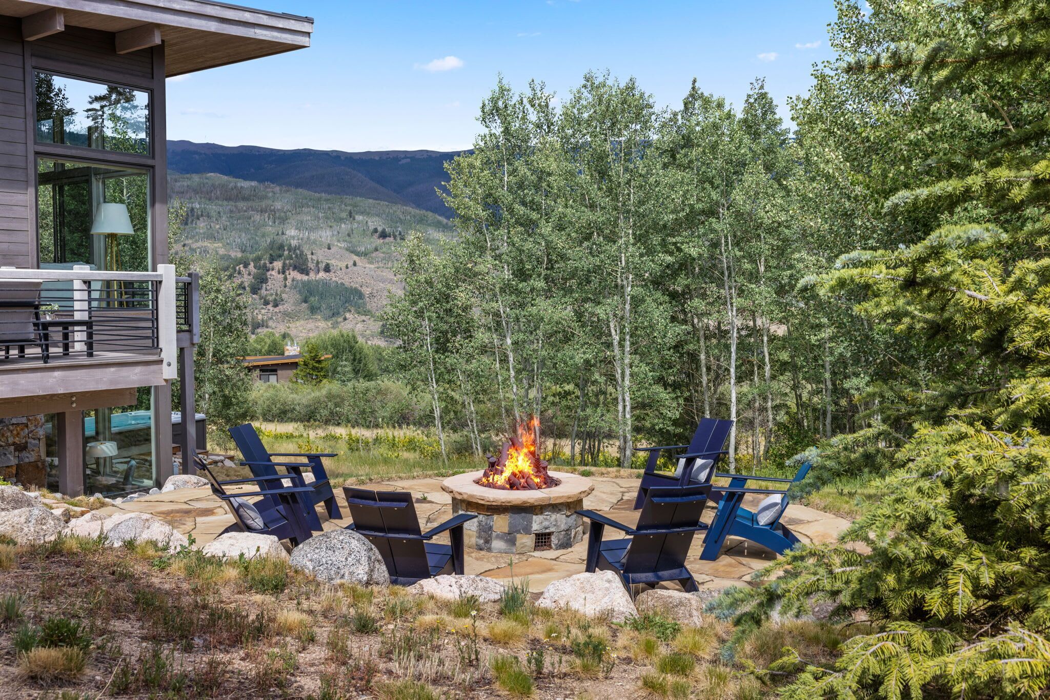 A deck with outdoor seating and a fire pit, surrounded by a mountainous landscape.