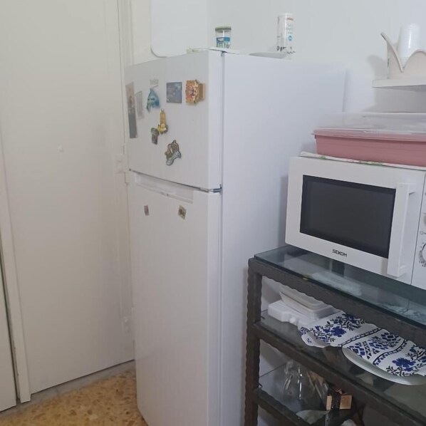 A kitchen with a white refrigerator, a microwave, and a glass-top table with dishes. - B&B TETYANa (Naples)