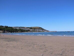 A beach with a town in the background, clear skies, and calm sea. - 73 Cildraeth (New Quay)