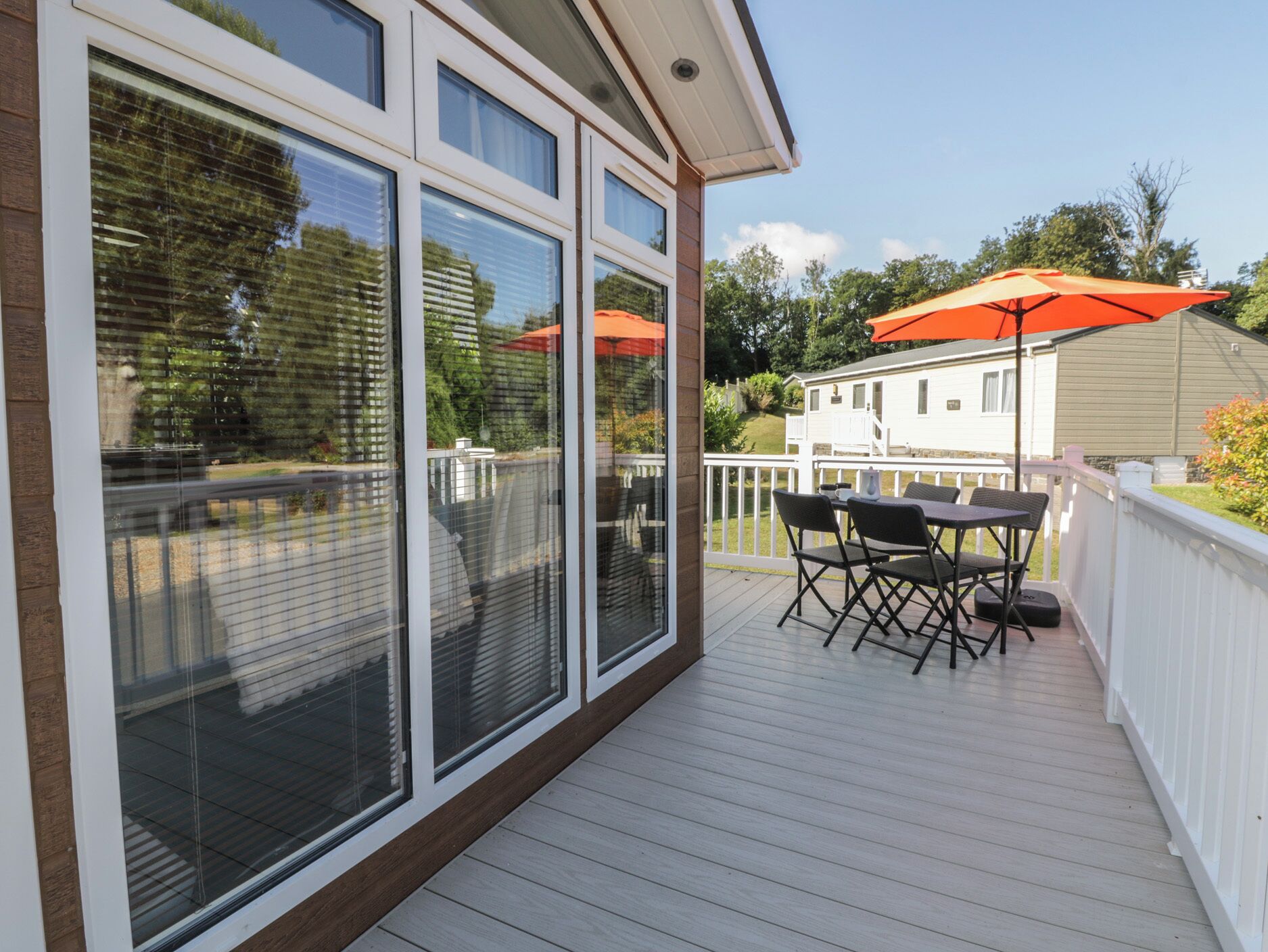 A covered deck with a table and chairs, large windows, and a white fence.