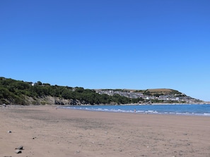 Een strand met een rotsachtige kustlijn, een heldere blauwe lucht en een stad op een heuvel in de verte.