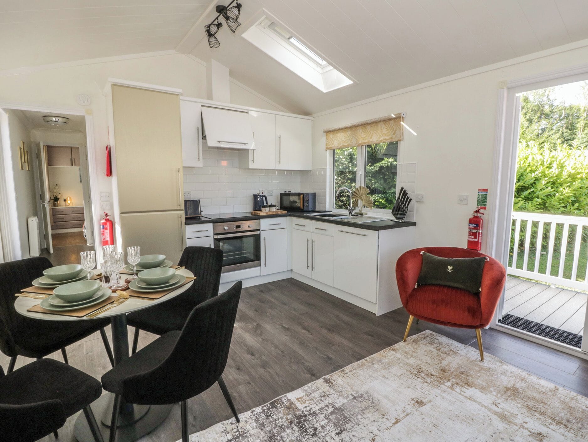A modern kitchen with white cabinets, a dining area with a round table and black chairs, and a red chair with a heart design.