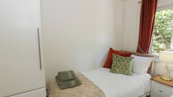 Un dormitorio con cama, mesita de noche, armario y ventana con cortinas.