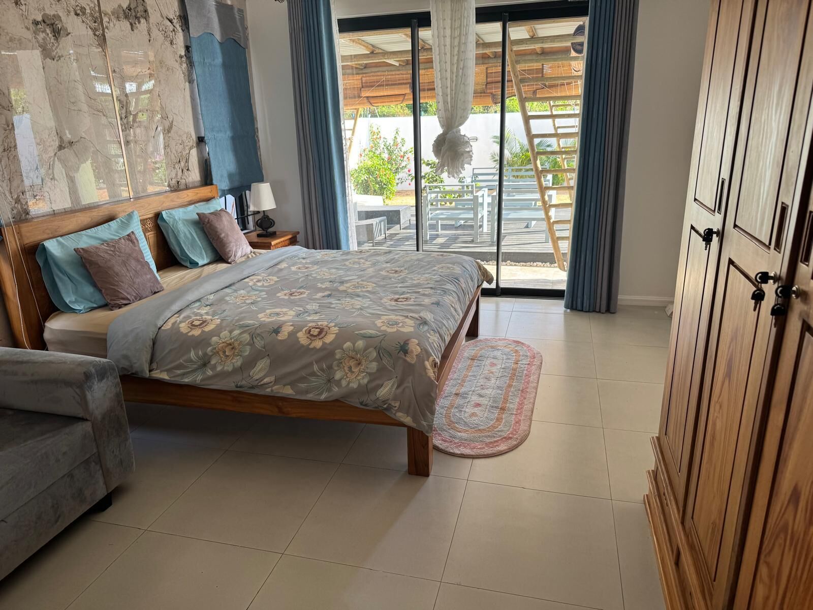 A bedroom with a bed, a nightstand, a wooden wardrobe, and a view of the outside through a sliding door.