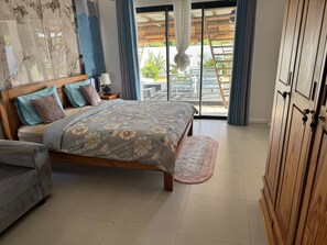 A bedroom with a bed, a nightstand, a wooden wardrobe, and a view of the outside through a sliding door.