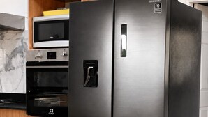 Un refrigerador Samsung de acero inoxidable con garantía de 10 años, un microondas encima y un armario de madera con un extintor.