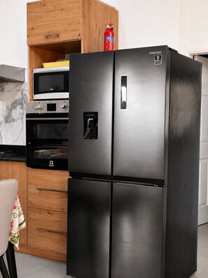 A stainless steel Samsung refrigerator with a 10-year warranty, a microwave above it, and a wooden cabinet with a fire extinguisher.
