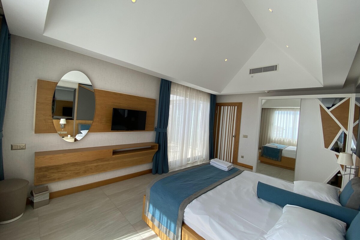 Une chambre d’hôtel moderne avec un grand lit, un téléviseur fixé au mur, un miroir et une armoire.