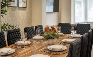 Mesa de jantar posta para seis lugares, com cadeiras estofadas pretas, uma planta no centro e copos de vidro transparente.