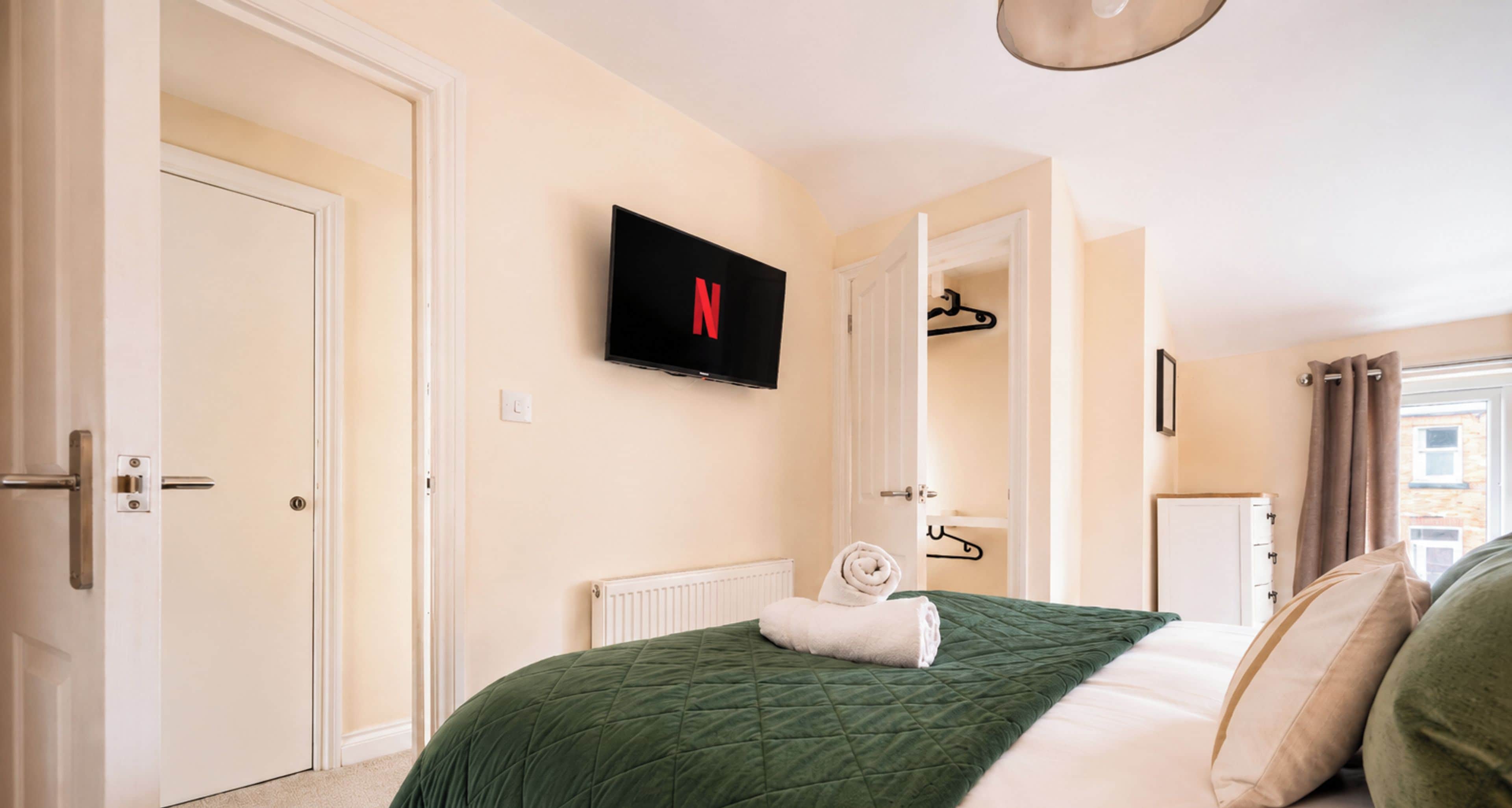 Ein Hotelzimmer mit einem Bett, einem an der Wand befestigten Fernseher und einer Tür zu einem weiteren Raum.