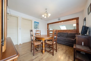 Un comedor con una mesa y sillas de madera, un sofá y un televisor sobre un mueble de madera.