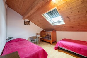 Un dormitorio con dos camas, una cuna de madera, un escritorio y un tragaluz.