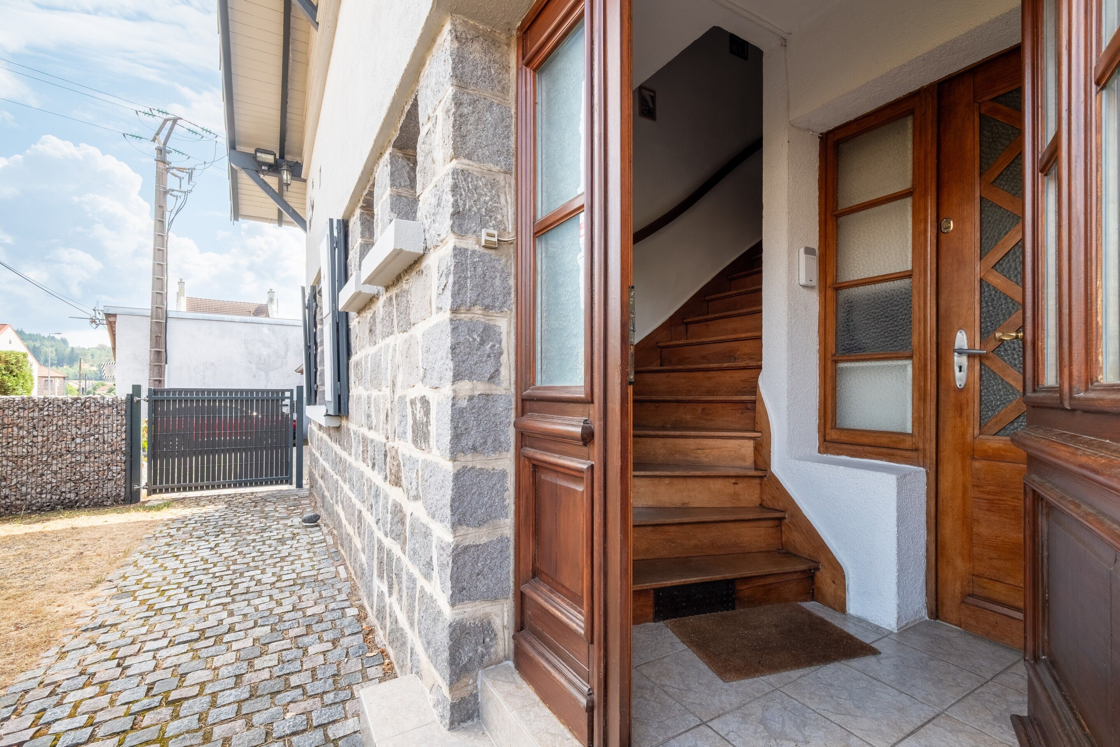 Un edificio de piedra con una escalera de madera que lleva a una puerta con paneles de vidrio esmerilado.