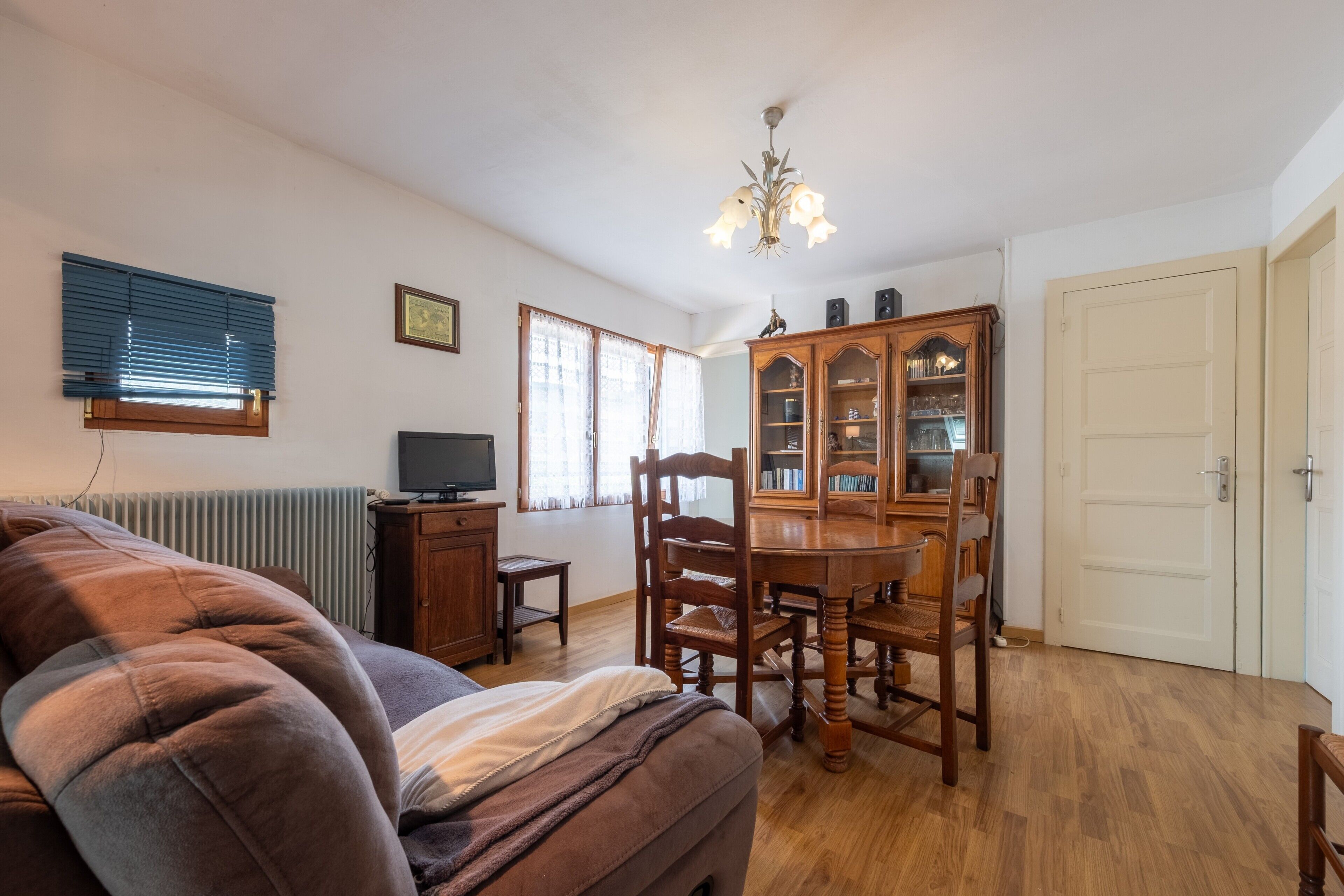 Un salon comprenant un canapé, un téléviseur, une table à manger avec des chaises, un buffet et un lustre.