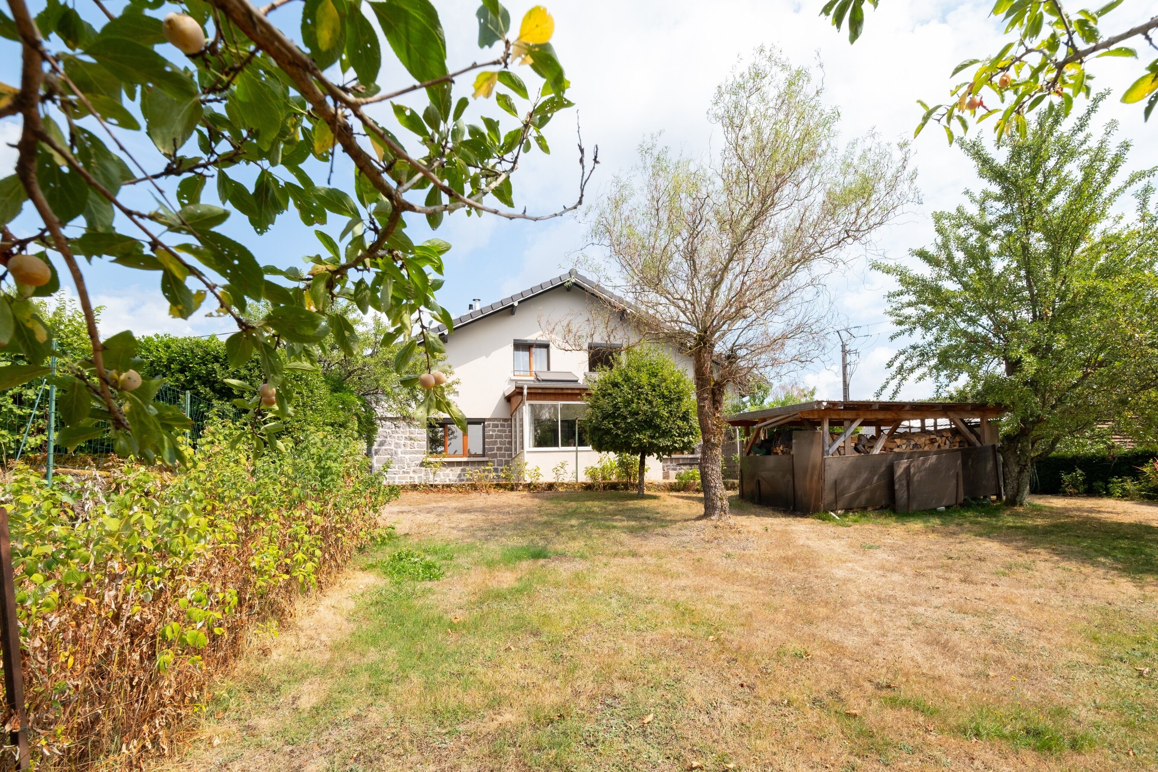 A house with a stone foundation, a wooden deck, and a fenced yard.