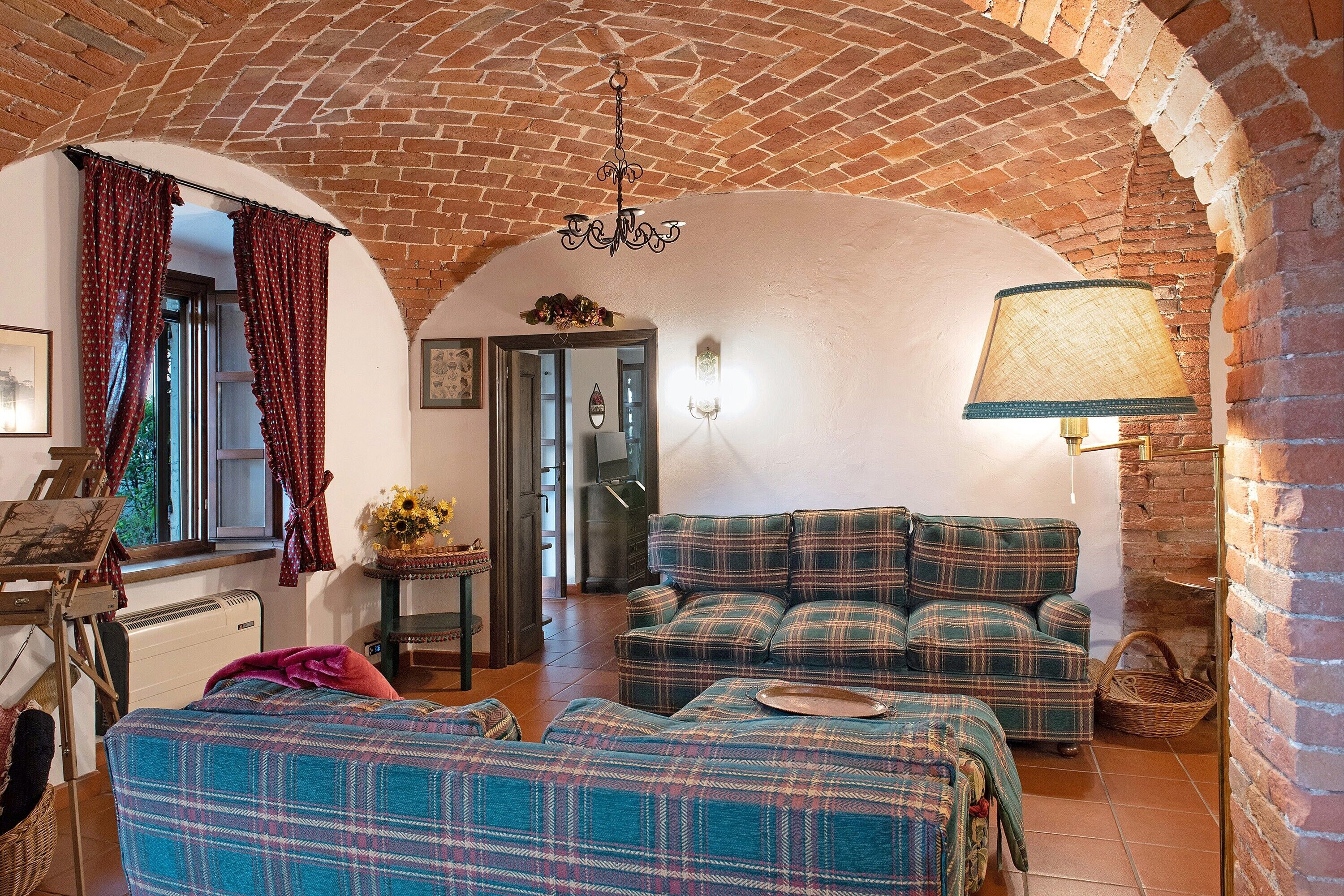 A cozy living room with a brick archway, a sofa set, a lamp, and a painting on the wall.