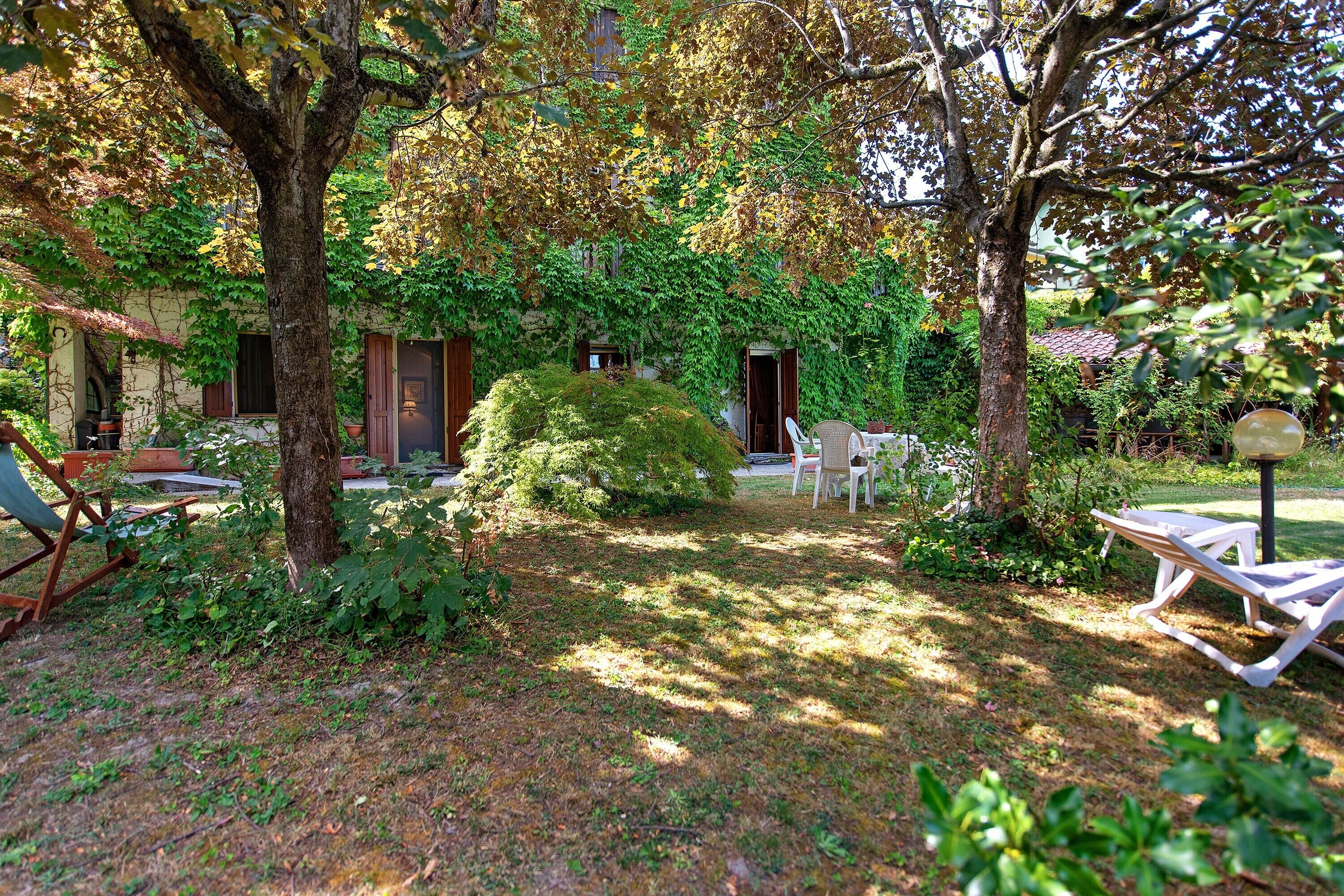 A garden with a wooden bench, a table, and a chair. There is a building with a door and windows.