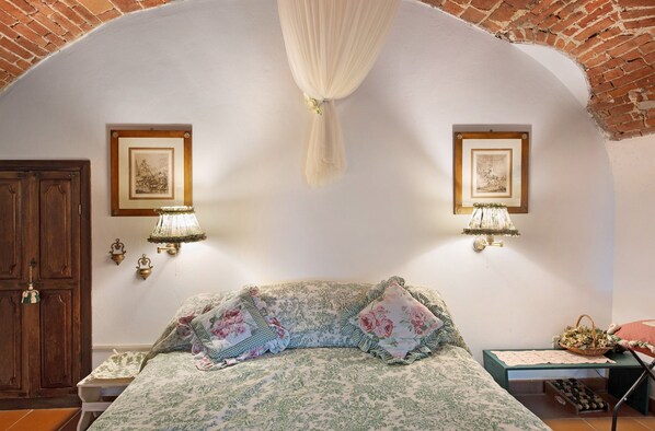 A bedroom with a bed, two wall-mounted lamps, a wooden door, and two framed pictures on the wall.