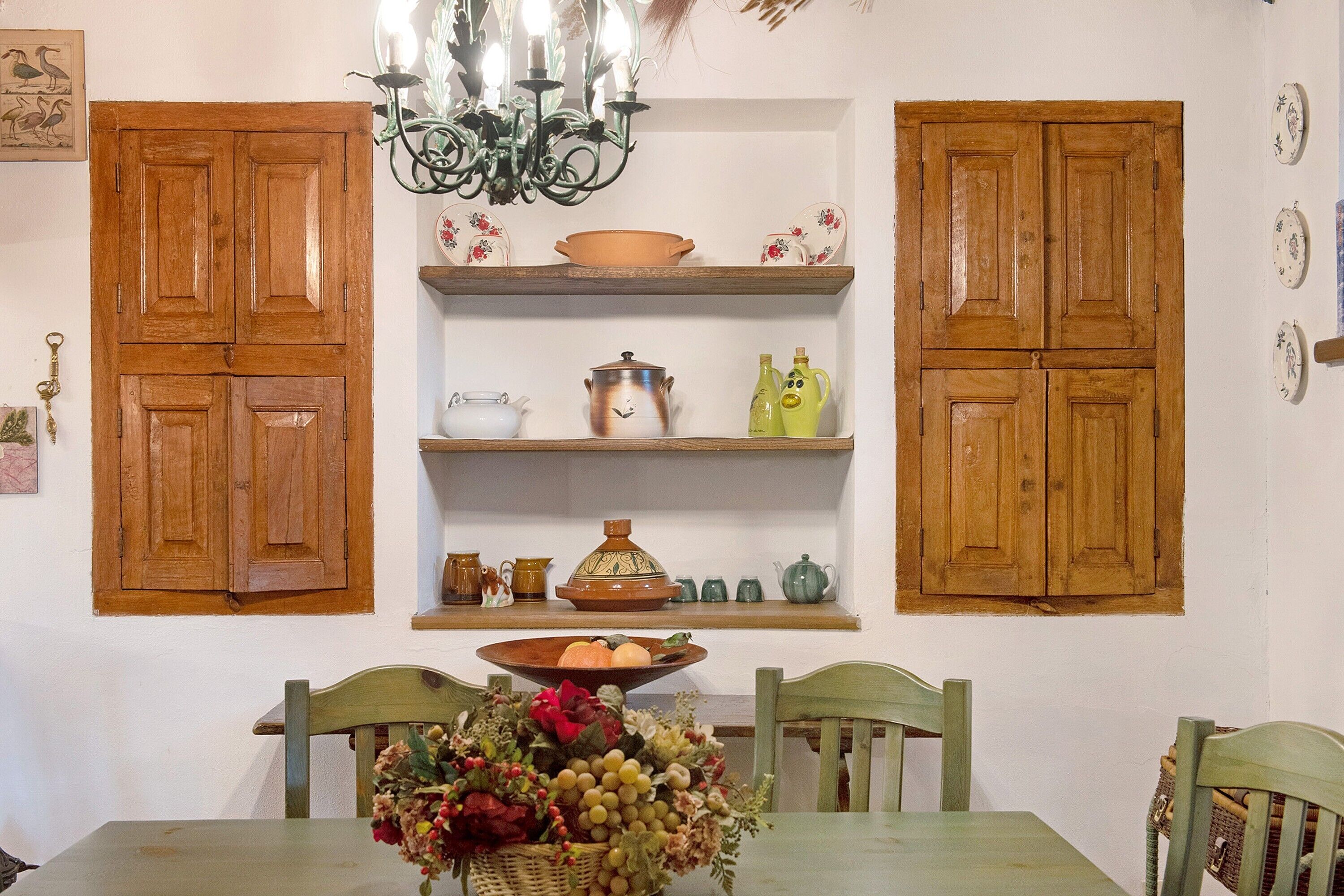 A dining area with wooden cabinets, a chandelier, and a table set with a fruit basket.