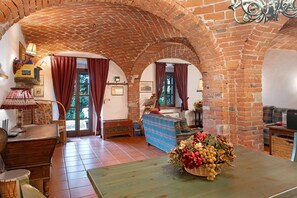 A room with a brick archway, a wooden table with a floral centerpiece, and a sofa with a plaid cover.