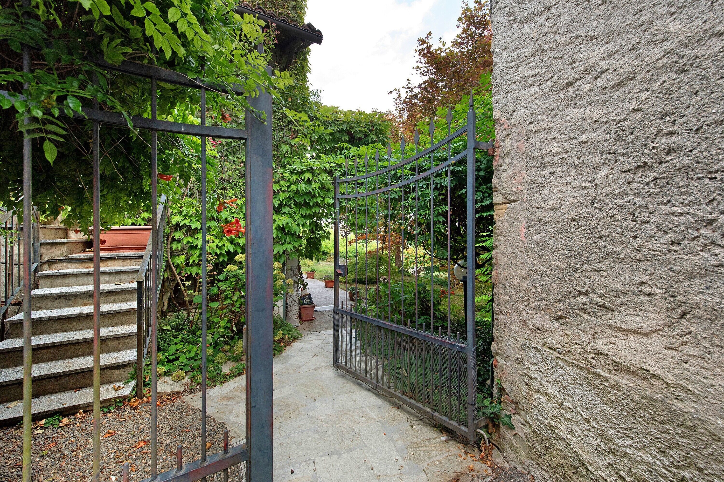 A narrow pathway flanked by a metal gate and a stone wall, leading to a staircase.