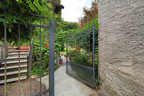 A narrow pathway flanked by a metal gate and a stone wall, leading to a staircase.