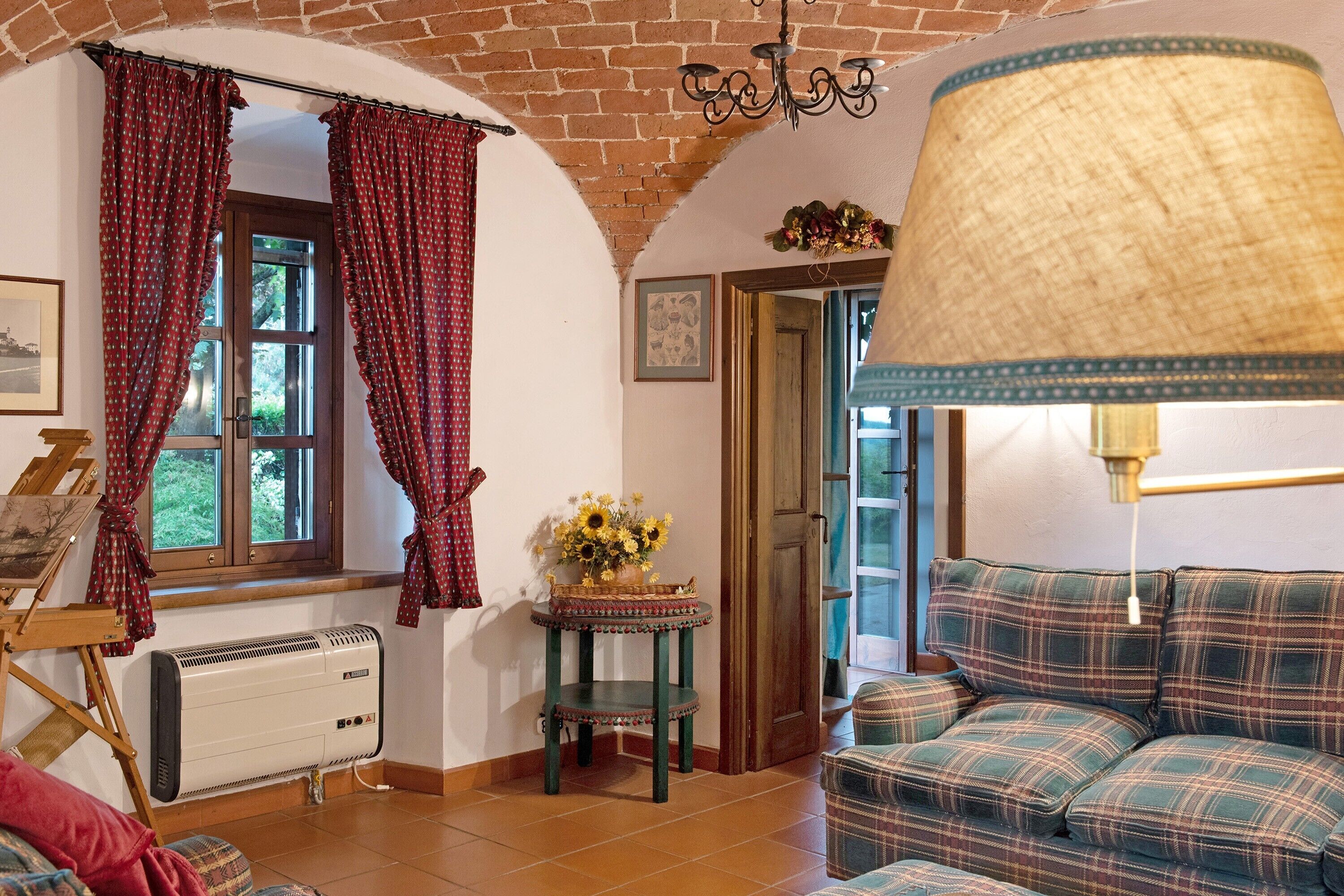 A cozy room with a brick ceiling, a fireplace, a sofa, a table with a vase of flowers, and a window with curtains.