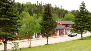 A red building with a sloped roof, a paved driveway, and a car parked in front. - Rocky Brook Acres (NL)