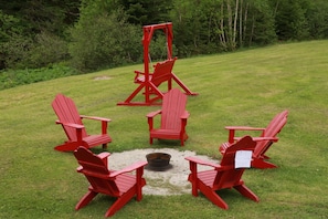 A set of red Adirondack chairs arranged around a fire pit in a grassy outdoor area.