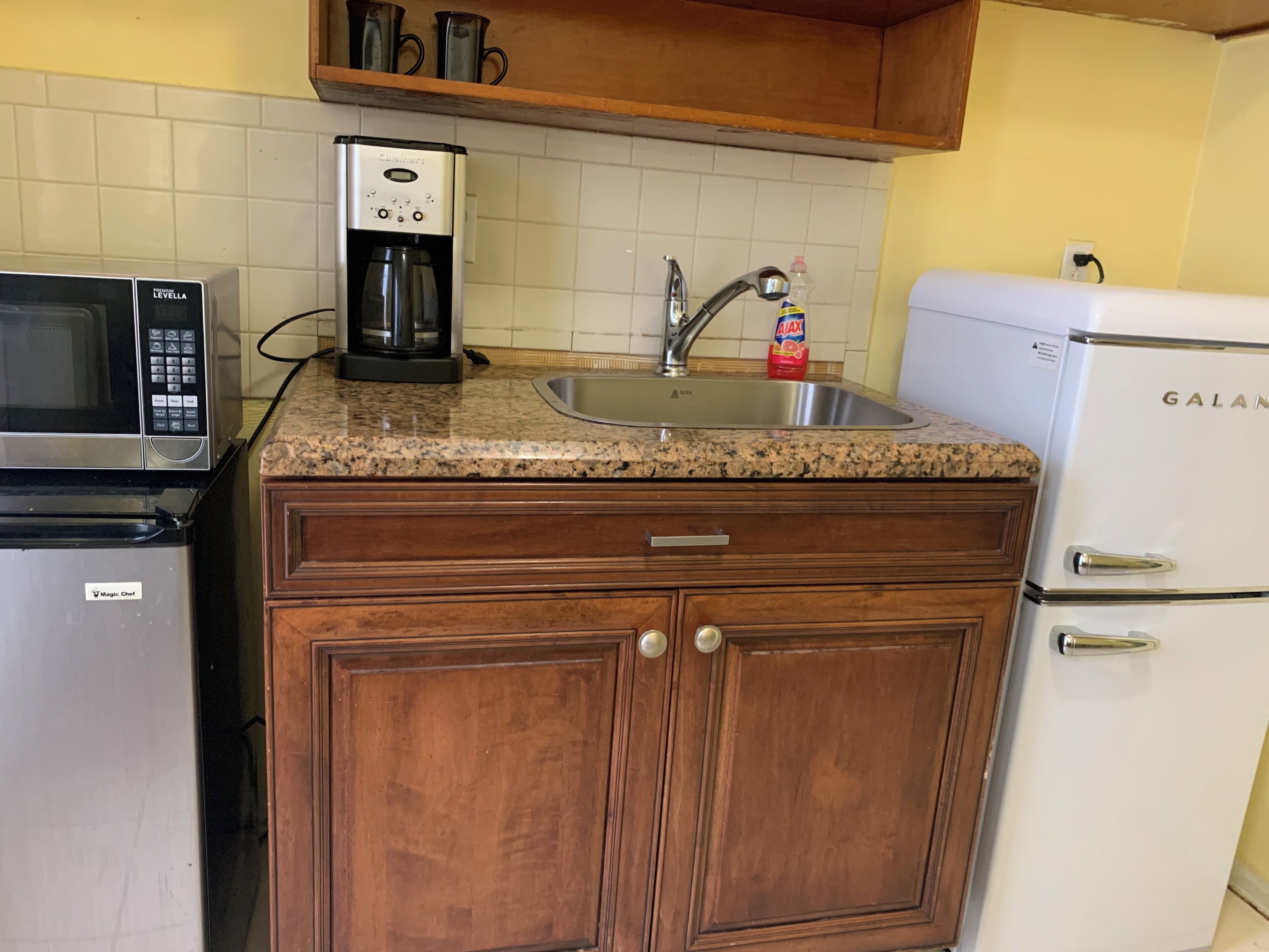 Una cocina equipada con microondas, cafetera, lavamanos y refrigerador.
