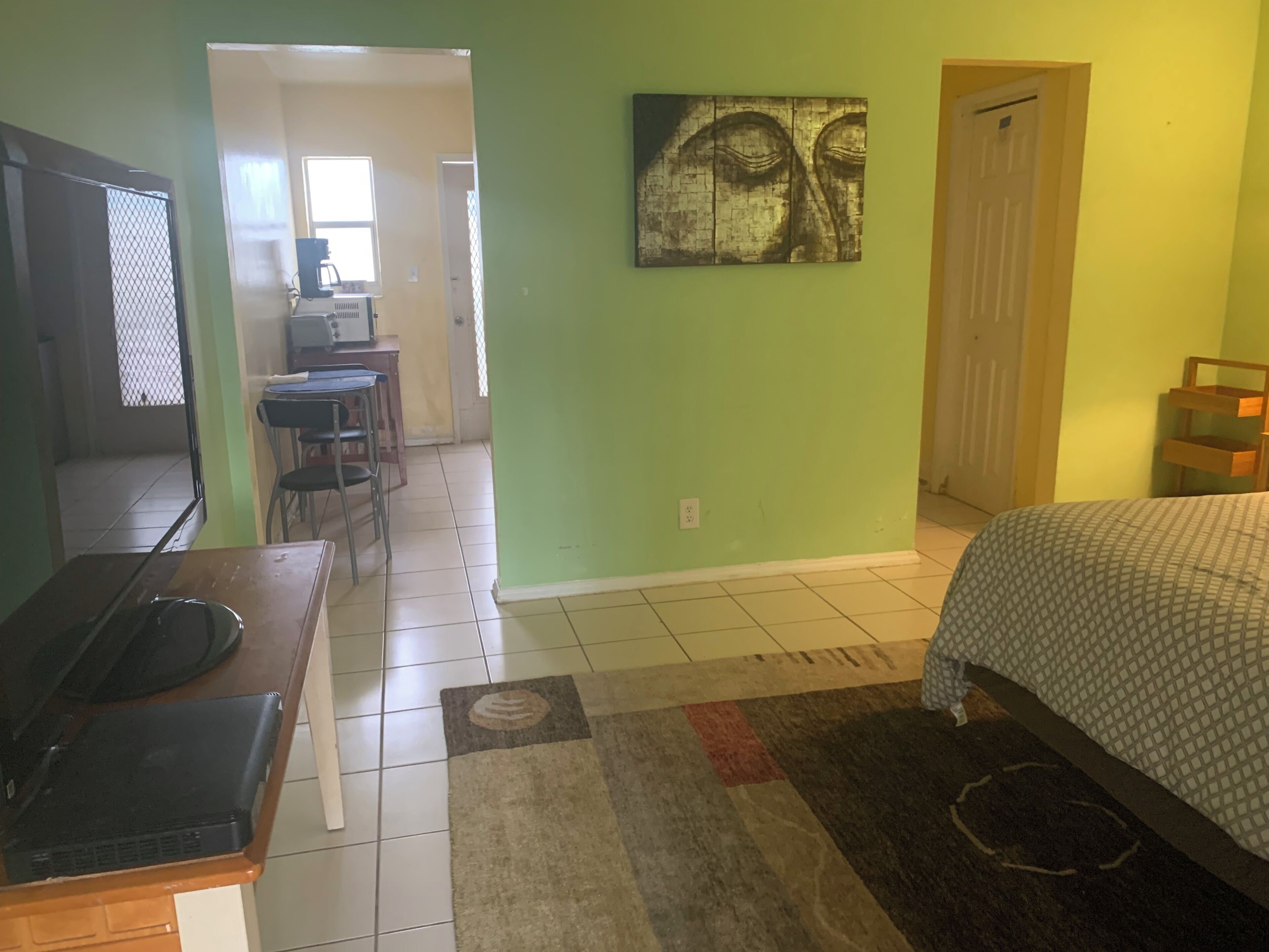 A room with a bed, a desk with a computer, a chair, and a door leading to another room.