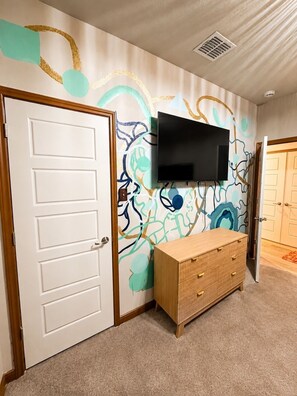 Ein Zimmer mit einem an der Wand montierten Flachbildfernseher, einem Holzschrank und einer schlicht gestalteten Tür.