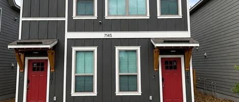 Un edificio residencial de dos plantas con fachada gris, detalles blancos y puertas rojas.
