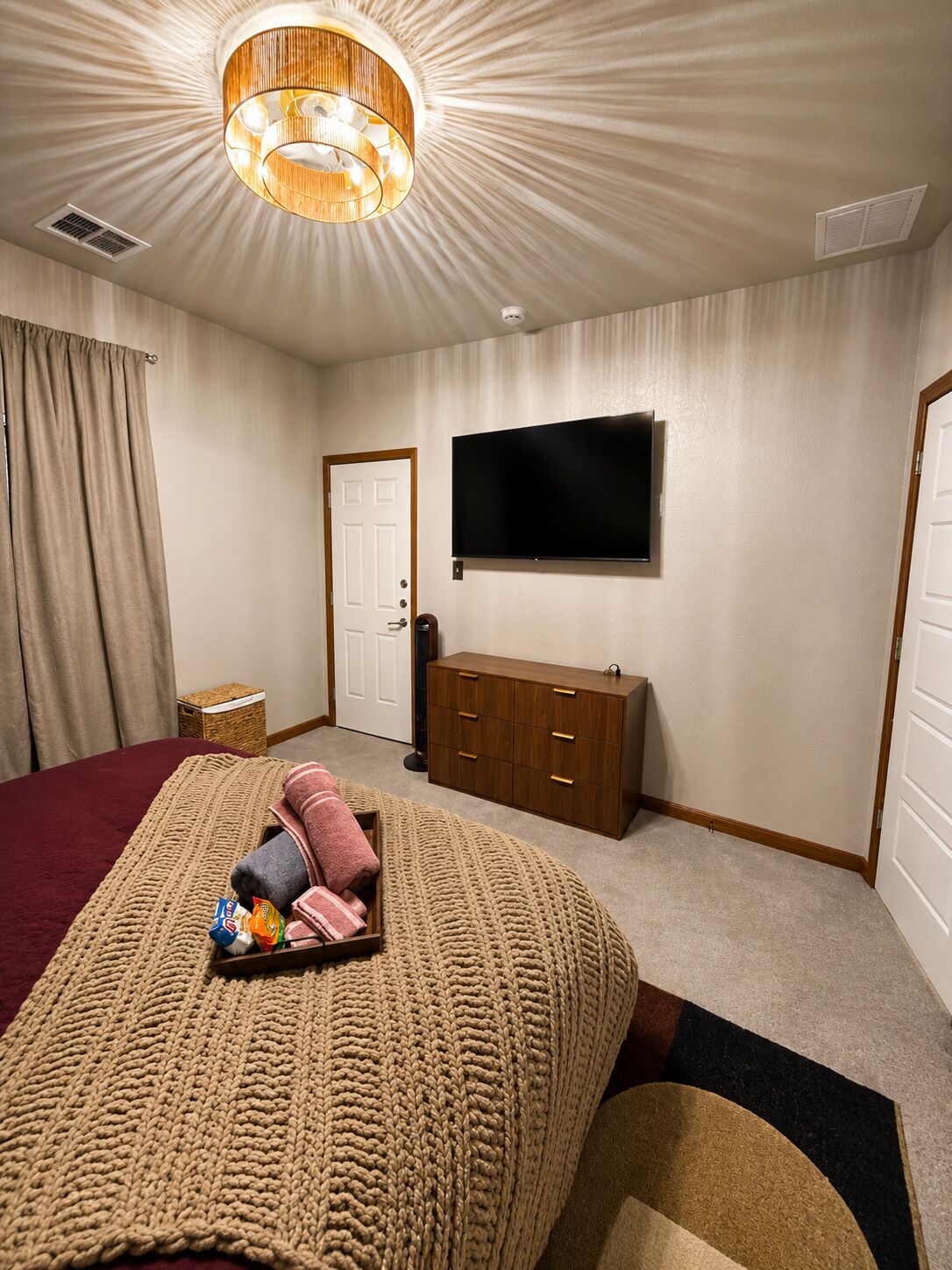 Une chambre d’hôtel avec un lit, un téléviseur fixé au mur, une commode en bois et un luminaire au plafond.
