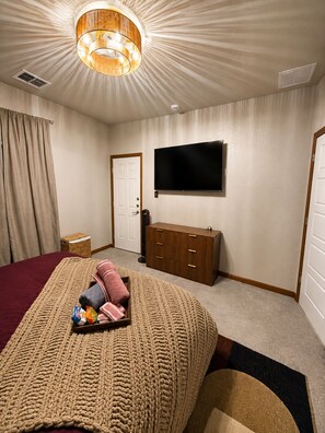 Ein Hotelzimmer mit einem Bett, einem an der Wand montierten Fernseher, einer Holzkommode und einer Deckenleuchte.