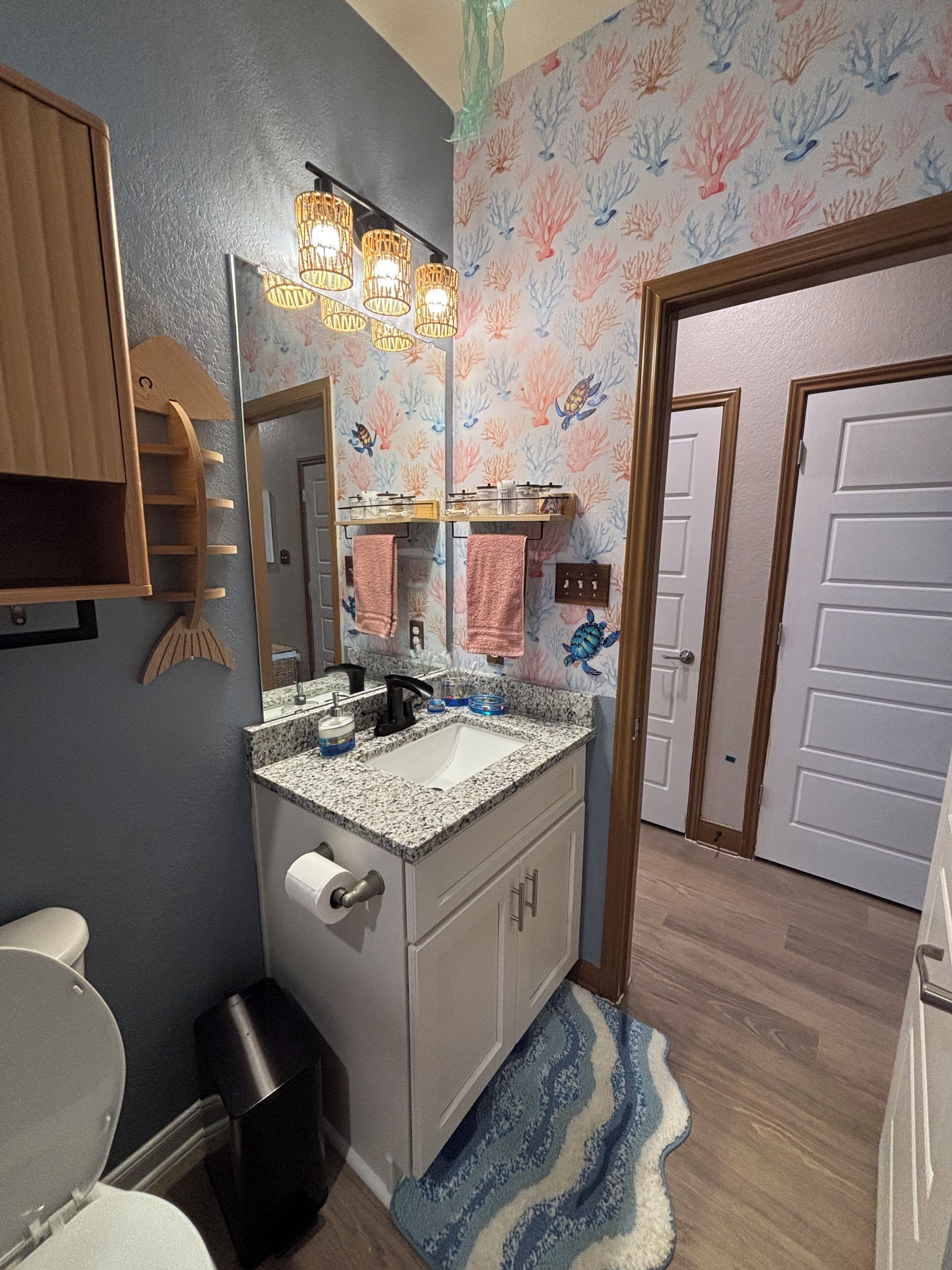 Un baño con lavamanos de encimera de granito, un espejo, toallero y zona de ducha.