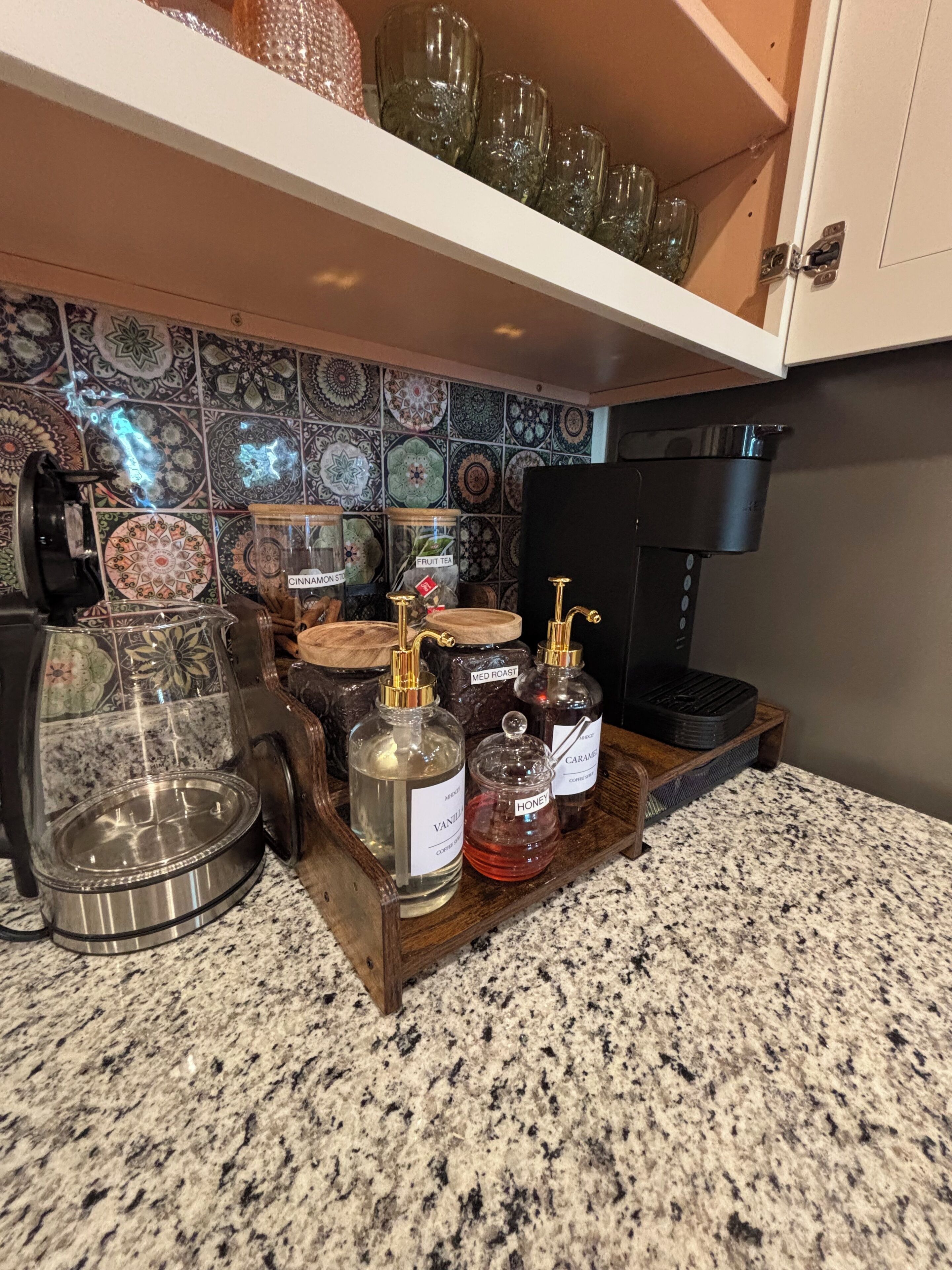 Una encimera de cocina con una cafetera, una jarra de vidrio y varios frascos de condimentos.
