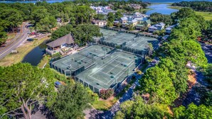 Luftaufnahme eines Tennisplatzkomplexes, umgeben von Wohngebäuden und einem See.