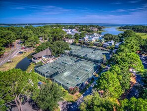 Luftaufnahme eines Tennisplatzkomplexes, umgeben von Wohngebäuden und einem See.