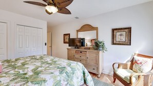 Ein Schlafzimmer mit einem Bett, einem Schminktisch, einem Fernseher, einem Sessel und einem Deckenventilator.