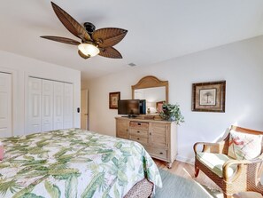 Ein Schlafzimmer mit einem Bett, einem Schminktisch, einem Fernseher, einem Sessel und einem Deckenventilator.