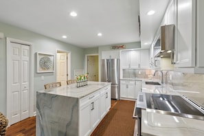 A modern kitchen with white cabinetry, a marble island, stainless steel appliances, and a brown rug.