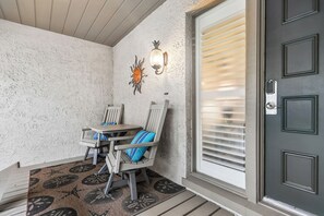 A covered porch with a table and chairs, a decorative wall, and a door with a peephole. - Gorgeous Villa w/ Panoramic Views (Hilton Head Island)
