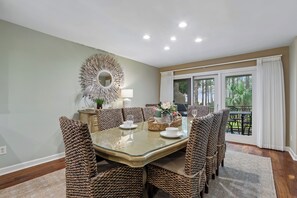 A dining area with a glass-top table, wicker chairs, a decorative mirror, and a view of the outdoors through a sliding glass door. - Gorgeous Villa w/ Panoramic Views (Hilton Head Island)
